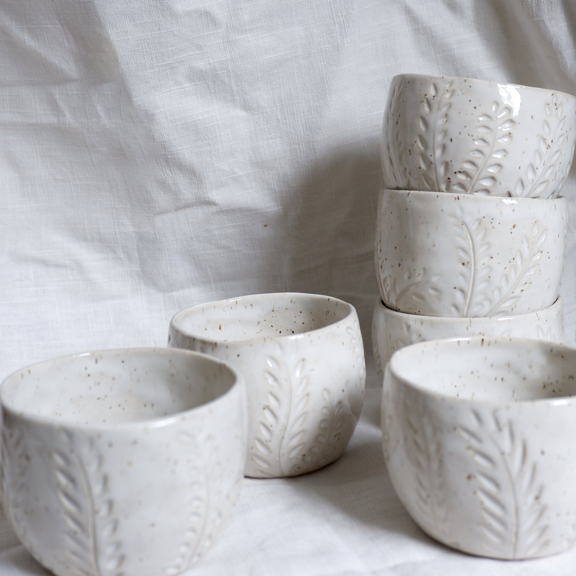 Set of white ceramic cups with leaf patterns on a white fabric background