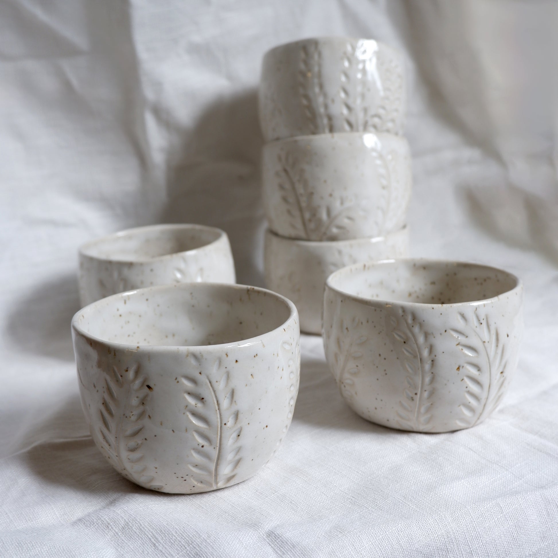 Set of white ceramic cups with textured design on a light fabric background
