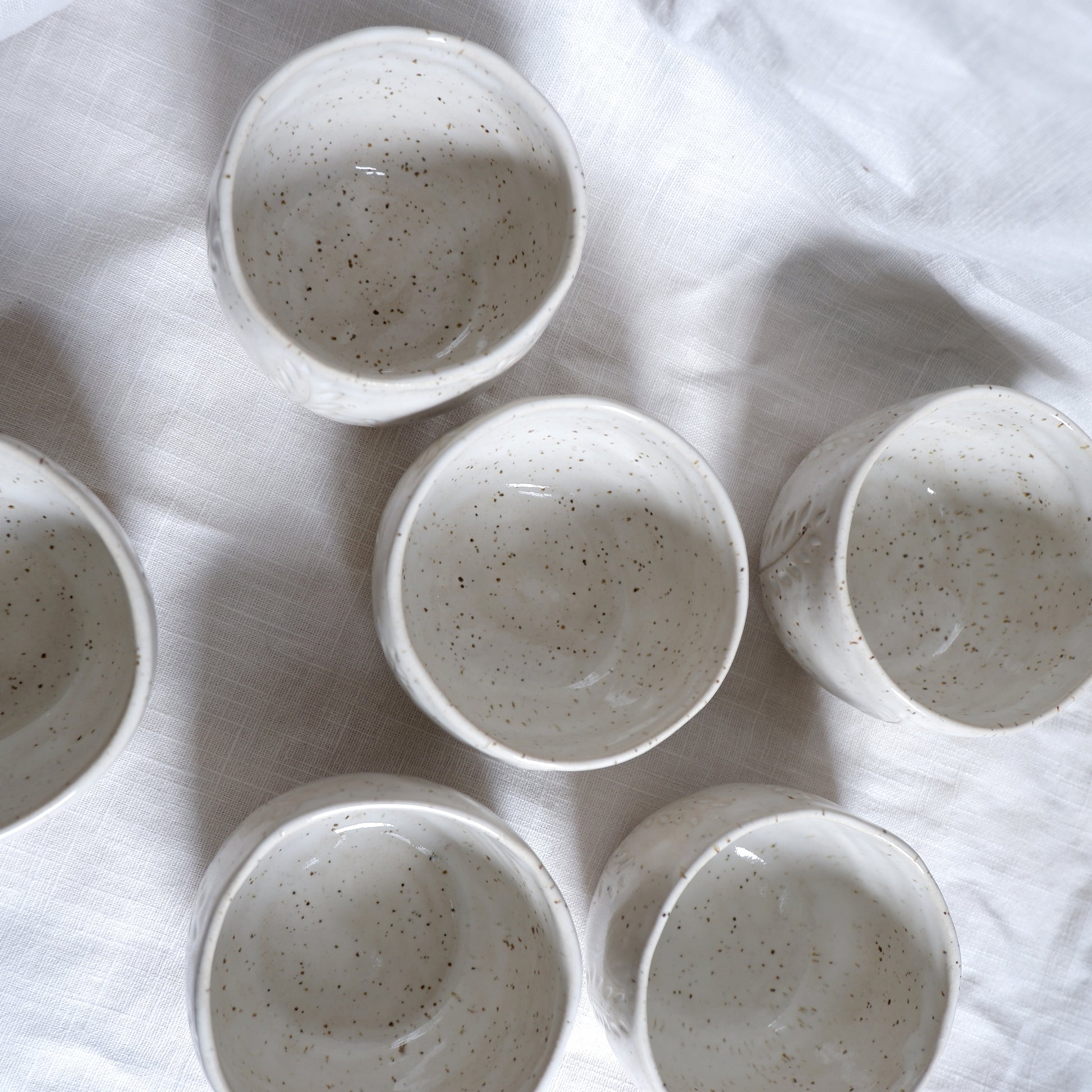 Set of ceramic cups with speckled texture on a white fabric background