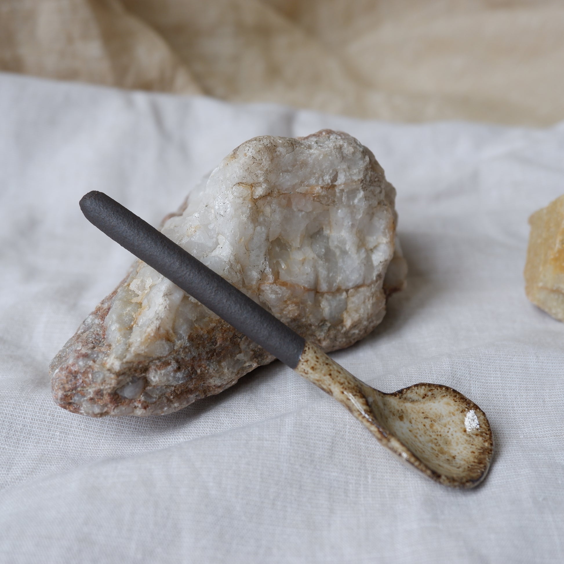 Small ceramic spoon with a black handle on a textured stone surface