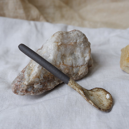 Small ceramic spoon with a black handle on a textured stone surface
