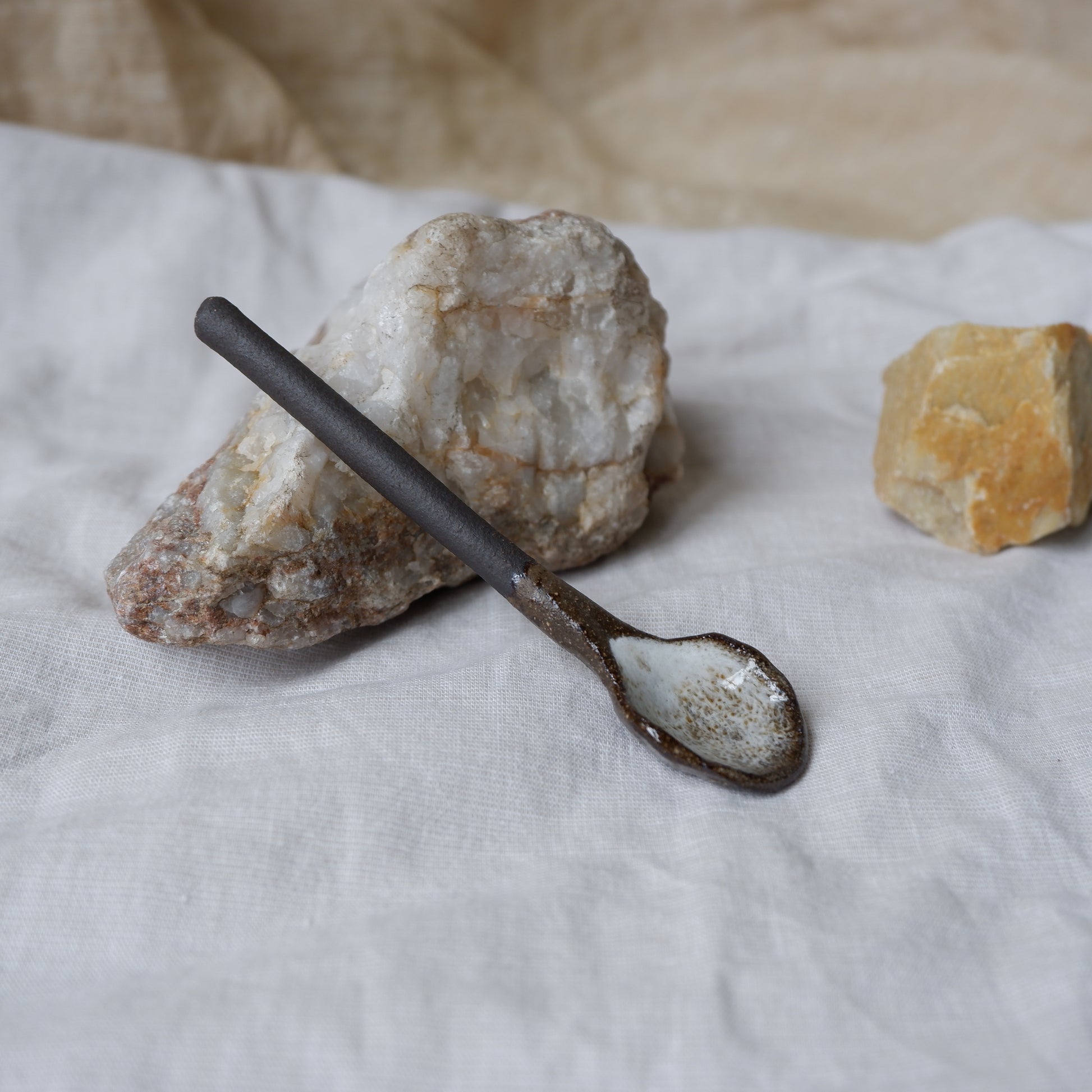 Decorative spoon with a rustic finish on a white surface with rocks in the background